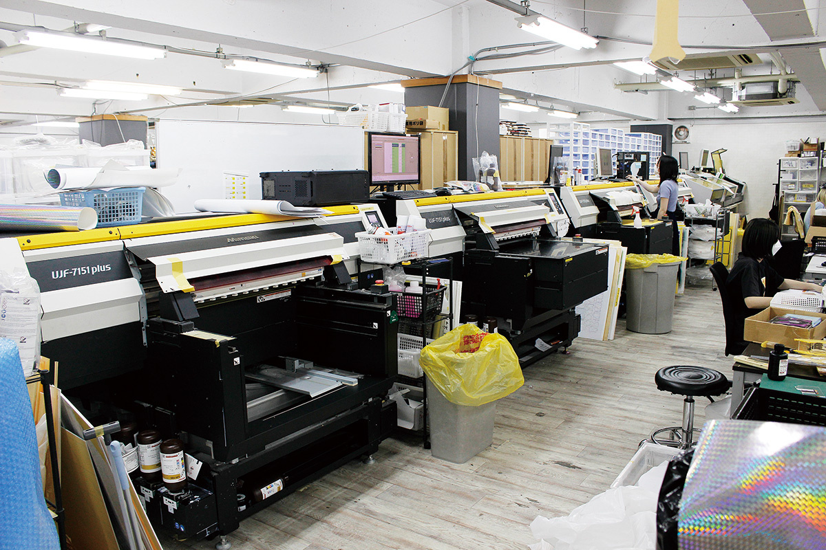 More than 40 UV printers, including Mimaki Engineering's UJF-6042MkII and UJF-7151 plus, are lined up in a row in SYNC INNOVATION's office.