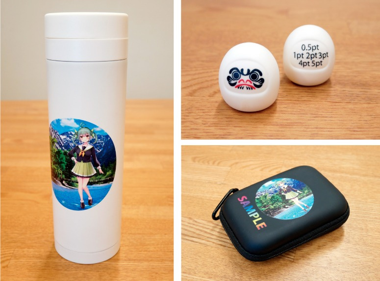 Various samples with transfer sheets applied, including a small daruma doll, coin cases, and bottles.